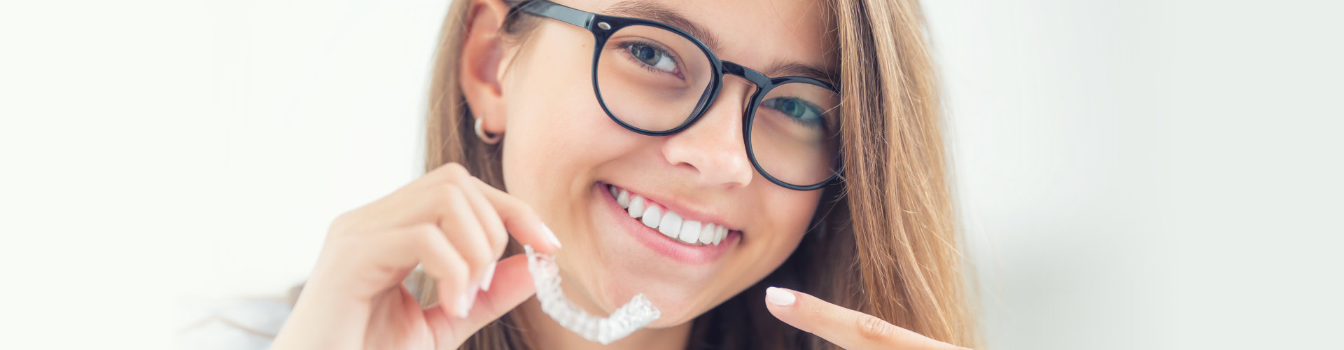 young woman smiling while holding her braces